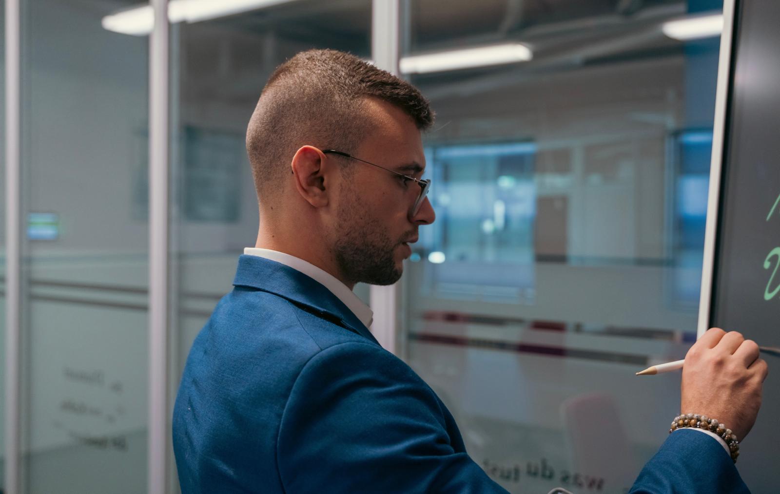 Berater im blauen Anzug notiert konzentriert an einer Glaswand im Büro.